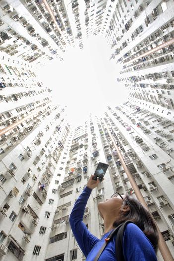 Low angle view of woman photographing on mobile phone by buildings in city
