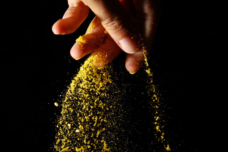 Close-up of hand sprinkling powder paint against black background