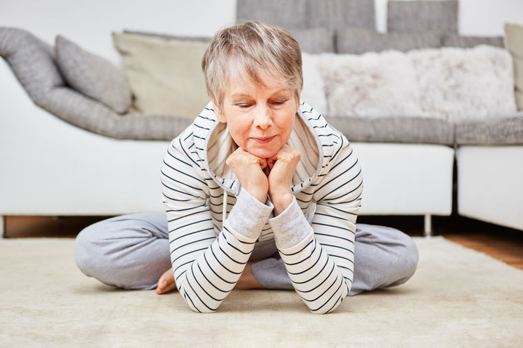 Senior woman sitting on carpet with hands on chin at home
