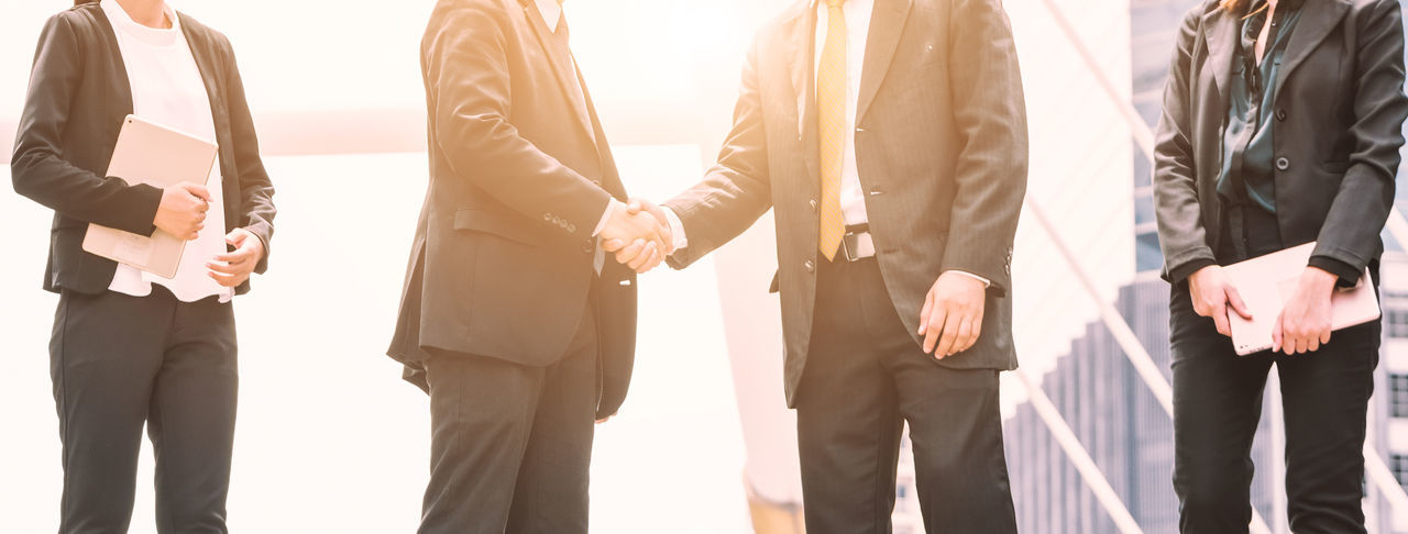 Midsection of businessmen shaking hands with colleagues in city