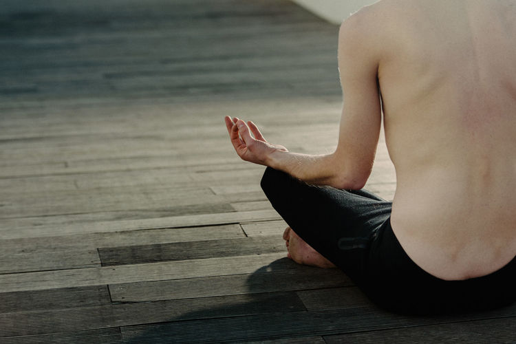 Low section of man meditating while sitting on wooden floor