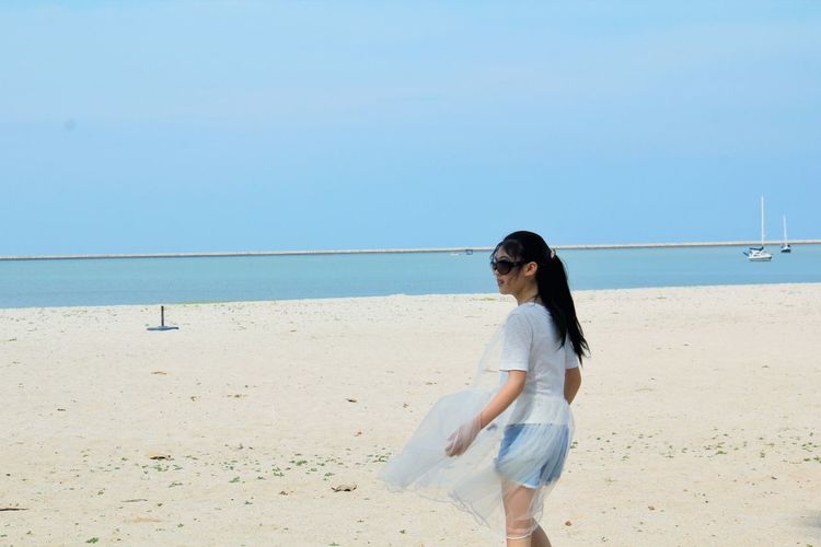 Girl standing at beach against blue sky