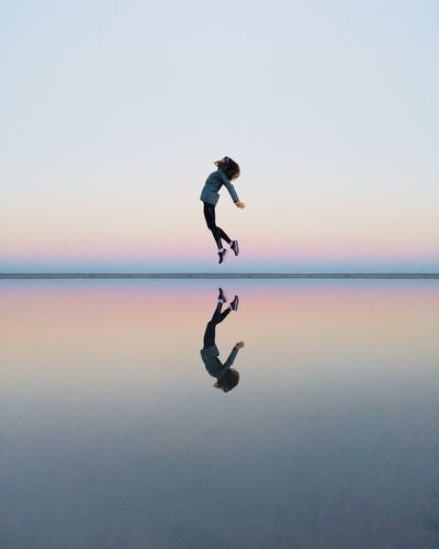 Full length of woman jumping on beach against sky during sunset