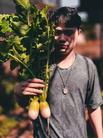 Young man holding radishes and standing outdoors