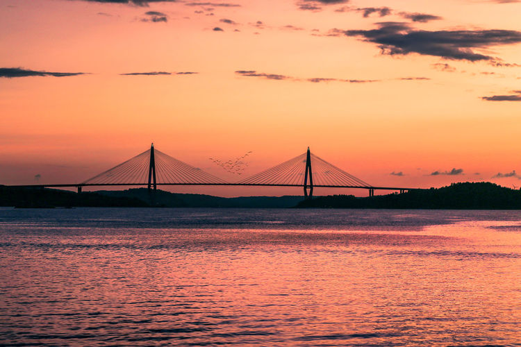 Bridge over calm sea against orange sky