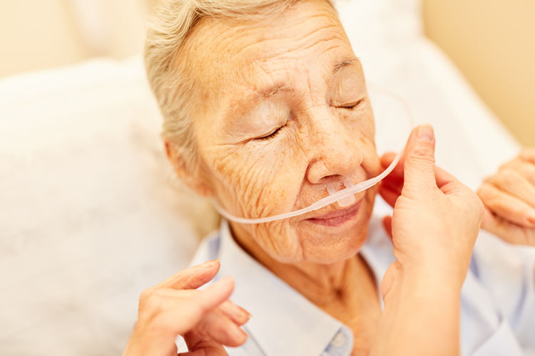 Close-up of cropped doctor adjusting medical supply on senior patient face lying on hospital bed