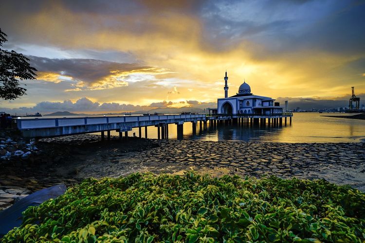 Great architecture of a mosque on the sea water during sunrise.