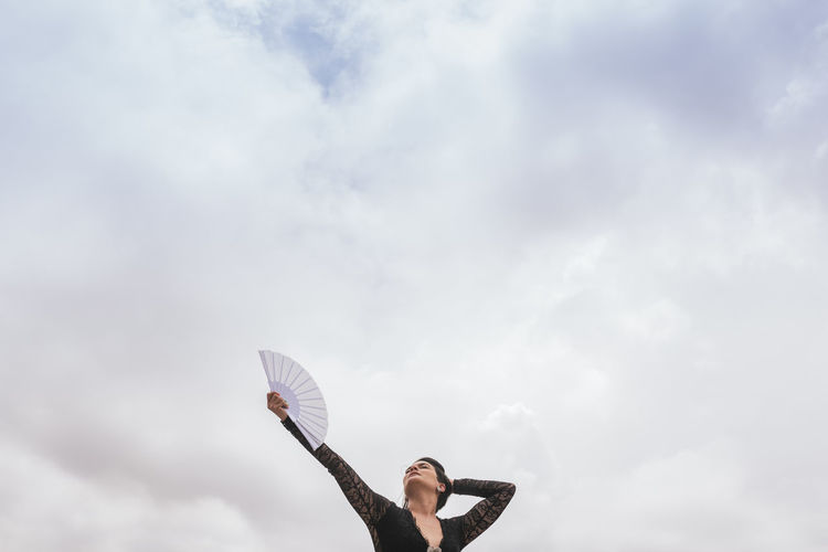 Female dancer with hand fan performing flamenco under cloudy sky