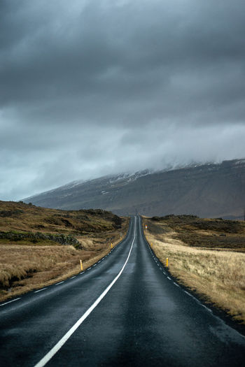 Empty road along landscape against cloudy sky