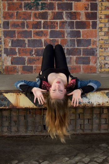 Portrait of young woman making face while lying on walkway