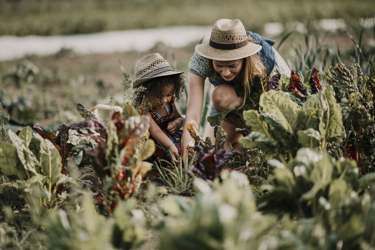 Female farm worker working while crouching by daughter at farm