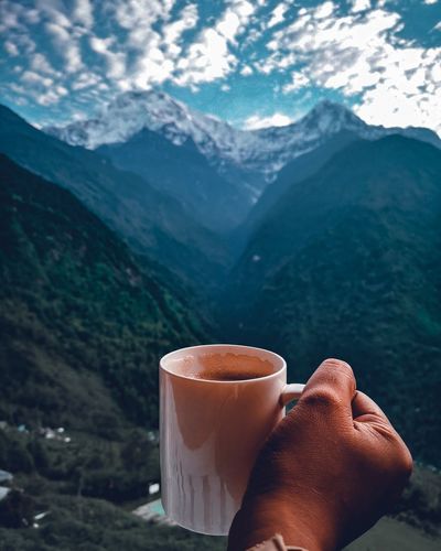 Cropped hand holding coffee mug against mountains