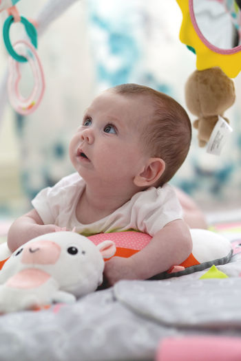 Portrait of cute curious newborn baby girl standing on belly playing and looking amazed of toys