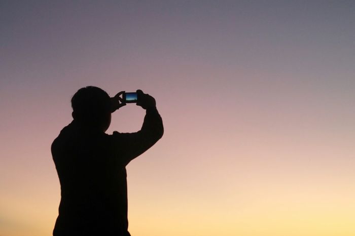 Silhouette man photographing clear sky at dusk