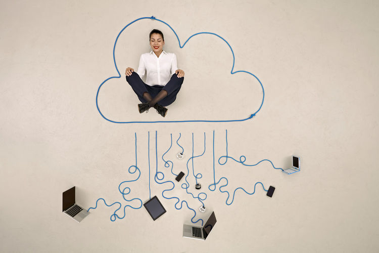 Businesswoman meditating in a cloud connected to mobile devices