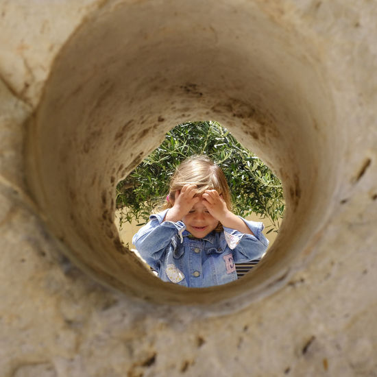 Girl with hand in hair looking down seen through hole