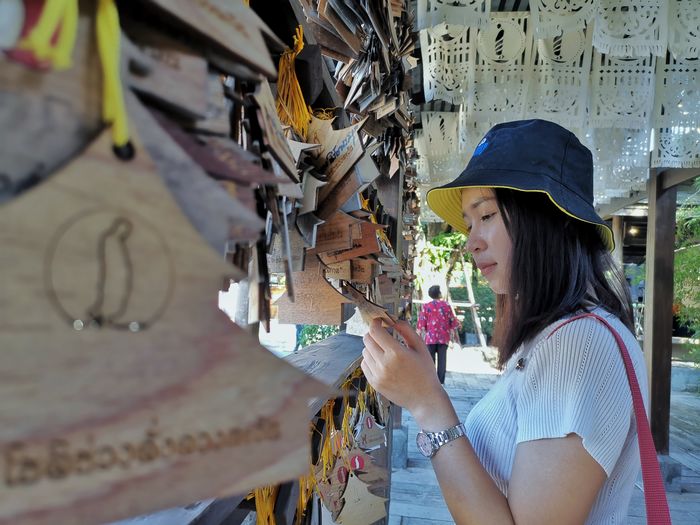 Side view of young woman wearing hat looking at prayer block at temple