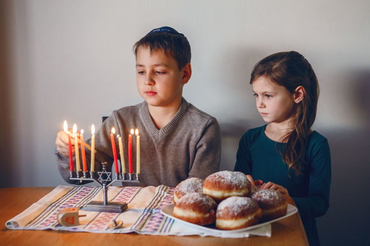 Brother and sister siblings lighting candles on menorah for jewish hanukkah holiday at home. 