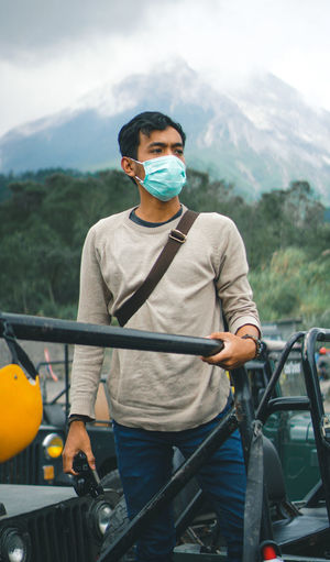 Portrait of young man with mask in car in front of mountain