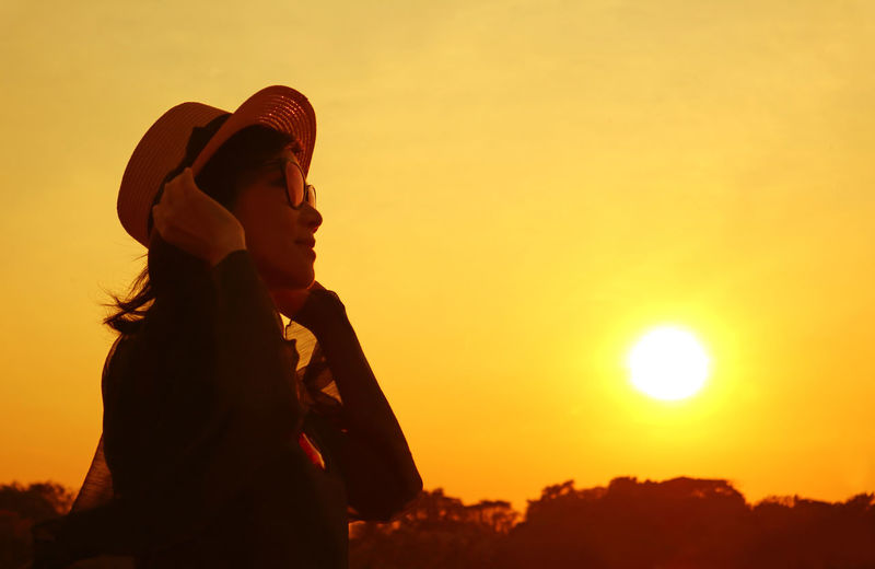 Side view of woman standing against orange sky during sunset