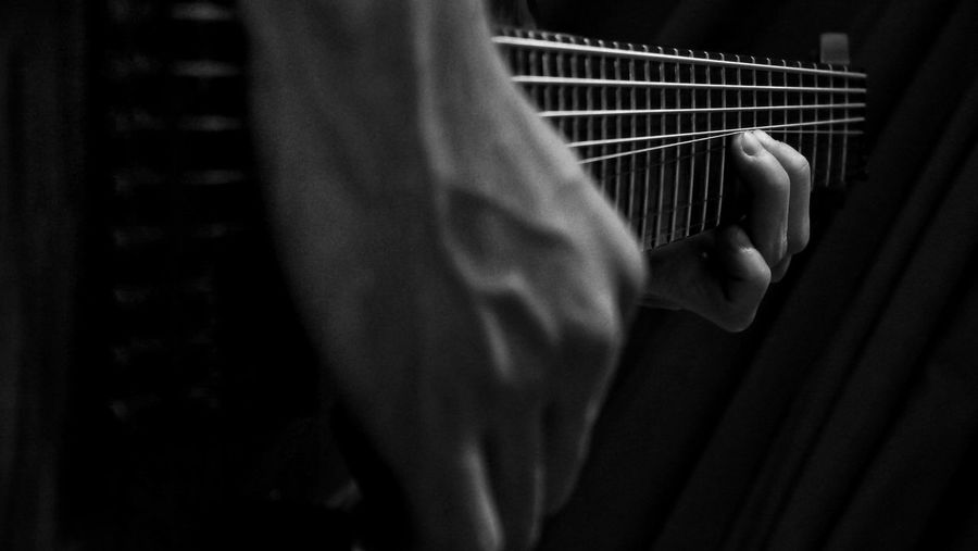 Cropped image of man playing electric guitar in darkroom