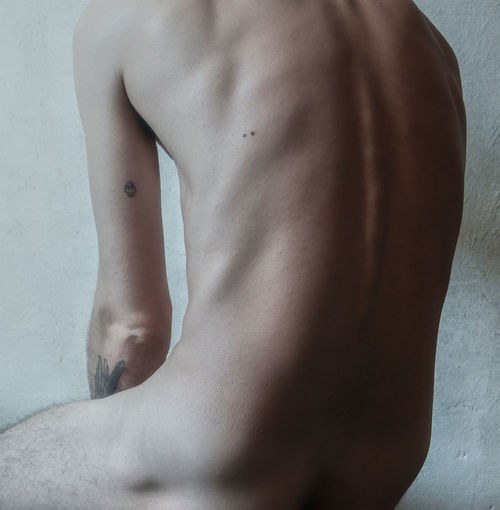 Midsection of sensuous naked man sitting against wall