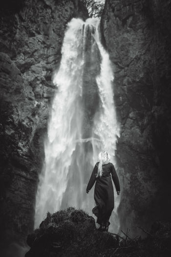Full length of young woman standing on rock against waterfall