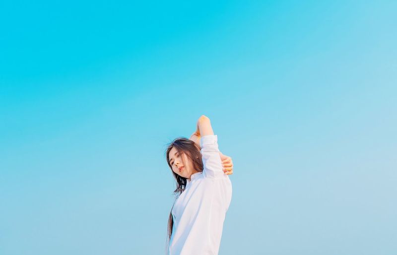 Low angle view of woman standing against clear blue sky
