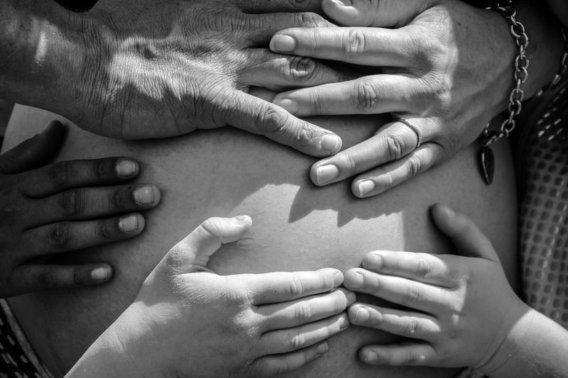 Cropped hands of people touching pregnant woman belly