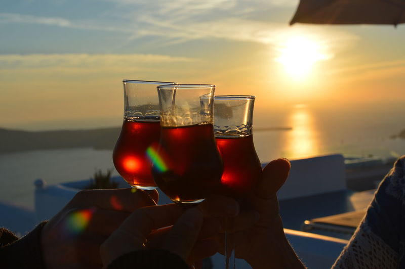 Close-up of hand holding wine glass against sunset