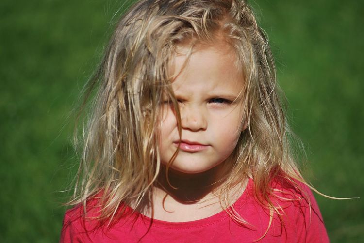 Close-up portrait of girl standing on grassy field during sunny day