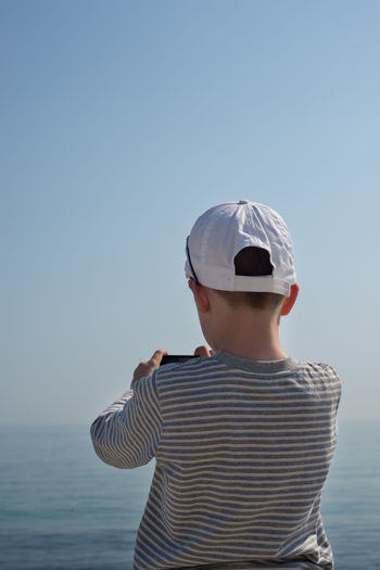 Rear view of boy standing by sea against clear sky