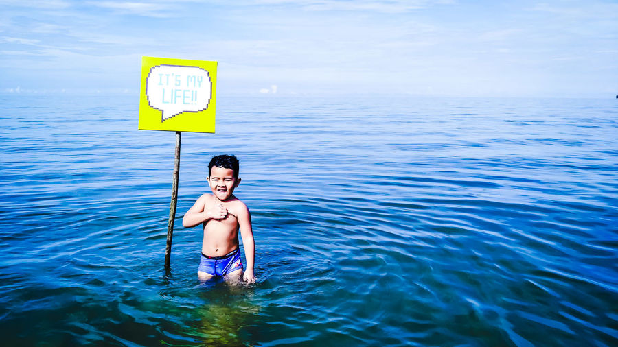 Little shirtless boy standing by sign in sea