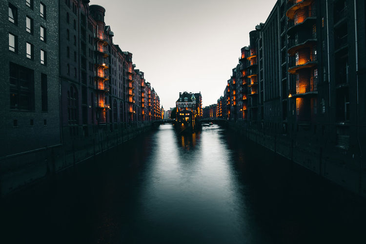 Canal amidst buildings against clear sky at dusk