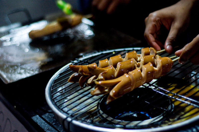 Cropped image of person cooking meat on barbecue grill