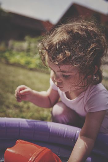 Girl playing in baby pool while sitting outdoors