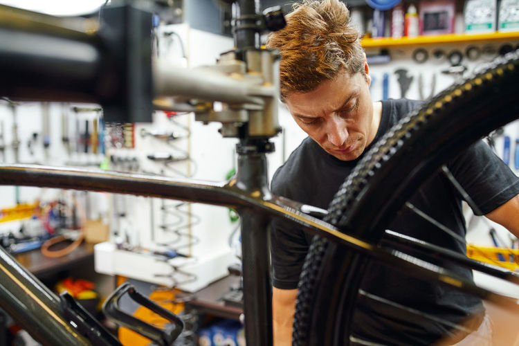 Focused male technician attaching wheel to bike while working in professional modern workshop