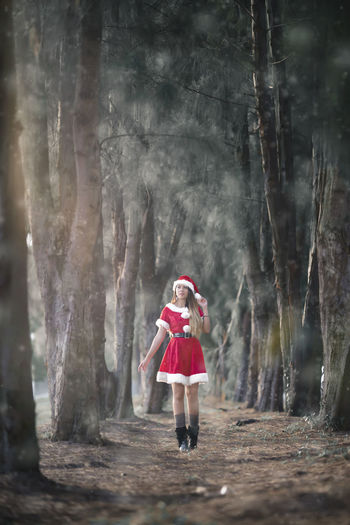 Full length of woman wearing santa hat walking amidst trees in forest