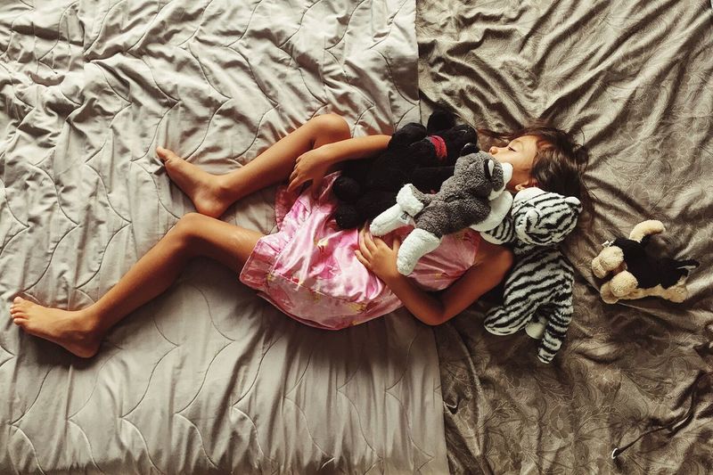 Directly above shot of girl with stuffed toys sleeping on bed at home