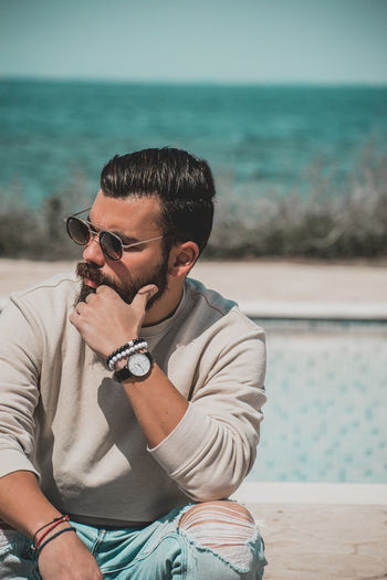 Young man wearing sunglasses sitting at sea shore