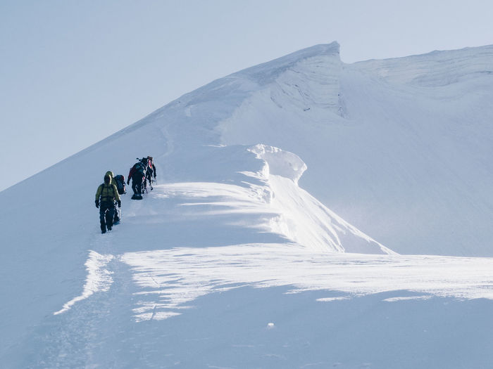 Low angle view of hikers walking on snowcapped mountain against clear sky