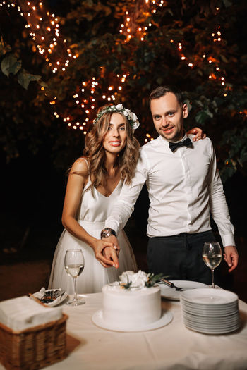 Portrait of couple standing by table with cake at night