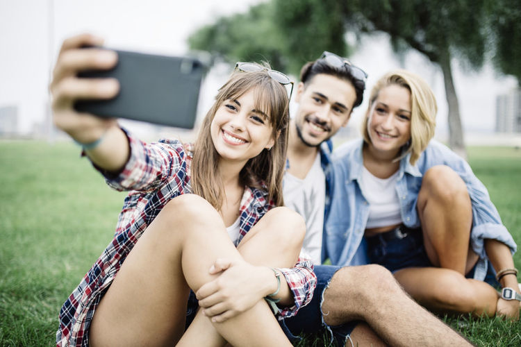 Smiling young woman with friends taking selfie on field
