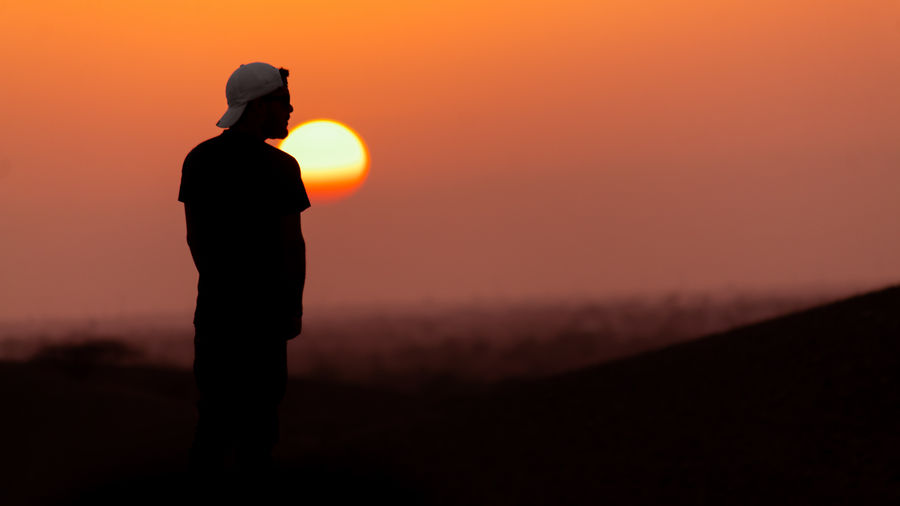 Silhouette man standing on land against orange sky