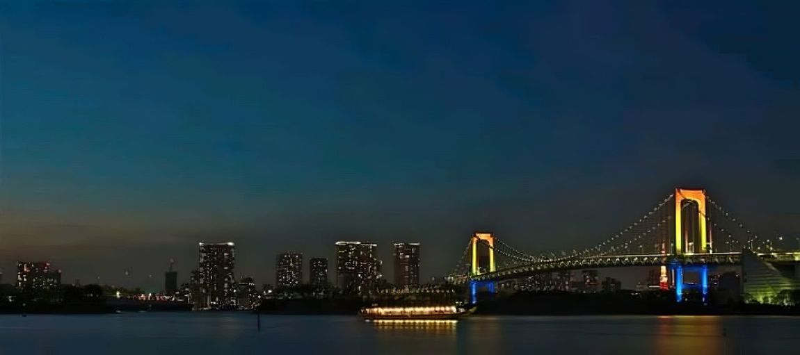 Illuminated bridge over river with city in background
