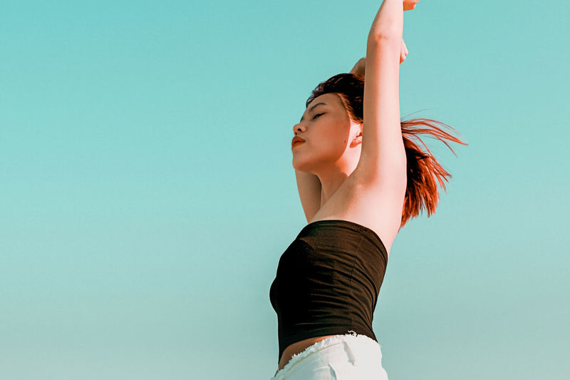 Low angle view of woman with arms raised and closed eyes standing against sky