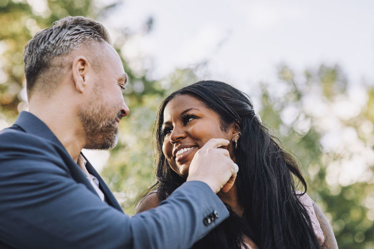 Smiling affectionate mature groom touching young bride's cheek