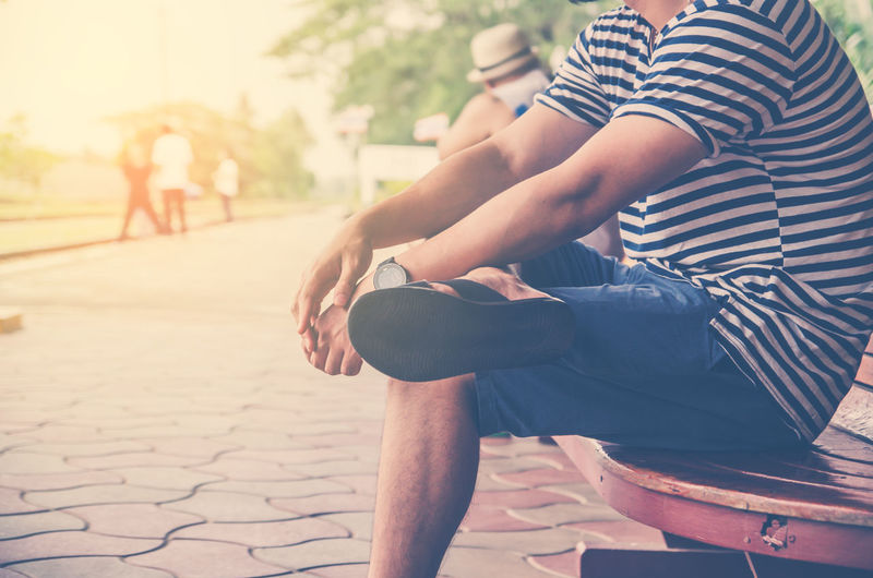 Low section of man with legs crossed at knee sitting on bench