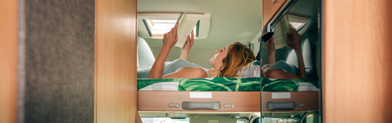Woman reading book lying on camper van bunk bed