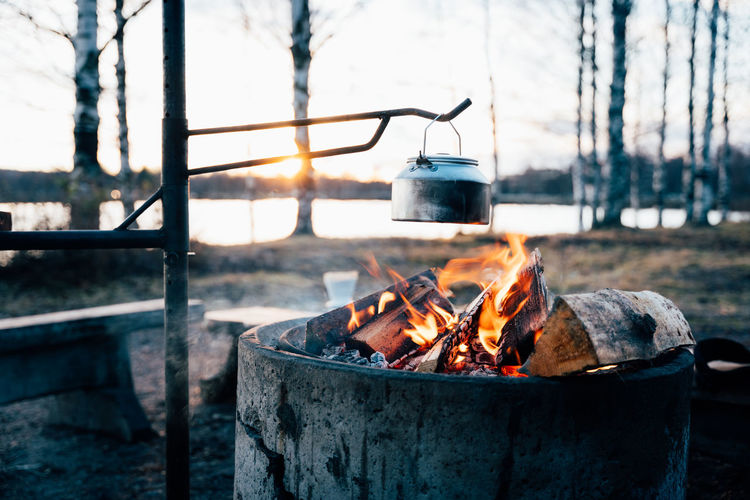 Cozy campfire with bright flame heating metal pot in woods in winter at sunset